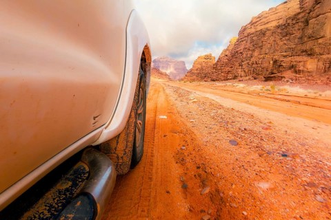 Close up 4wd vehicle driving across Wadi rum red sand track with desert mountains off road