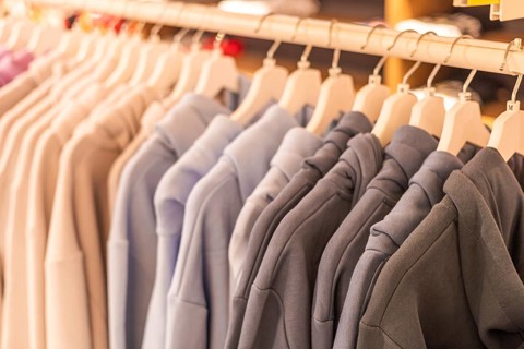 Hoodies displayed on hangers in a retail store. Various colors include gray, blue, and beige. The