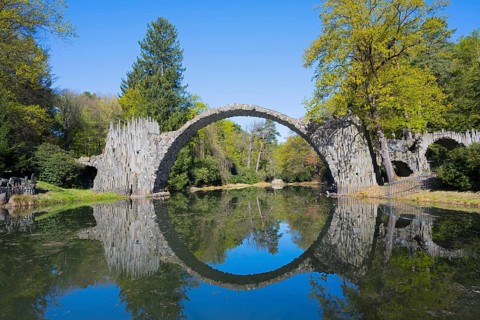 Perfect reflection of the stone bridge on the calm water, surrounded by forest, Rakotz Bridge,