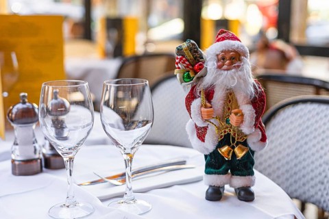 A festive table setting with two wine glasses and a decorative Santa Claus figurine. The scene