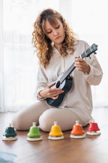 A woman in white focused on playing a ukulele with colorful bells
