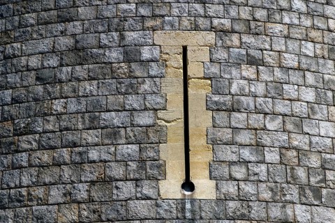 A tall narrow archery window is set into the coursed stonework of a curved tower at Windsor Castle,