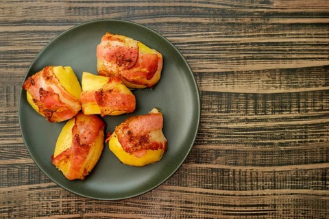 Top view of plate with roasted potatoes wrapped in bacon on wooden table