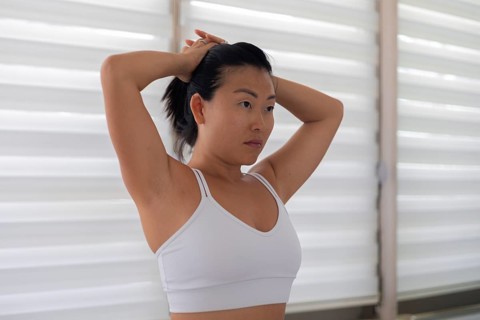 Woman with hands behind head appearing calm, standing by blinds