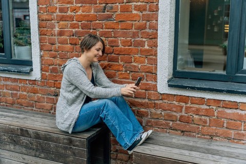 Smiling Woman Using Smartphone on a Wooden Bench, A woman casually sits on a bench using her