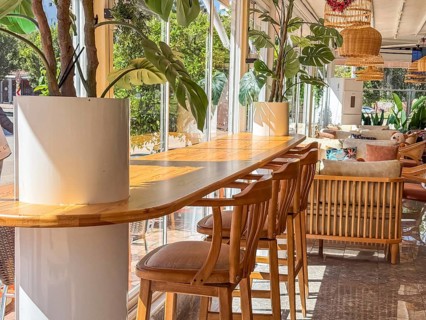 A modern restaurant interior with wooden tables and chairs. The space is bright and airy, featuring