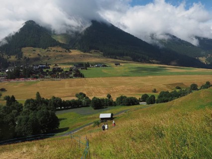 Rural scenery of a valley with fields and a village surrounded by wooded hills and mountains,