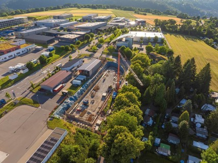 Aerial view of a construction site with a crane, surrounded by industrial areas and nature. Clear