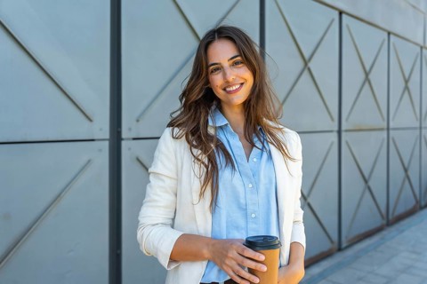 Young businesswoman smiling confidently, looking at camera while holding a disposable coffee cup