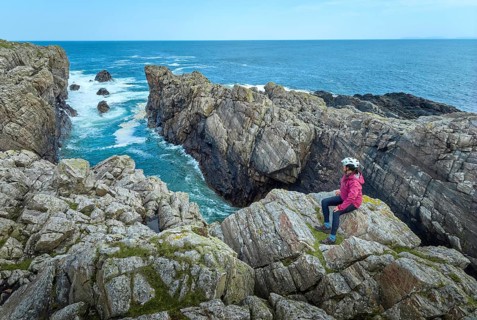 Nice senior woman resting during a bicycle tour in the rocky cliffs of Strathy Point in northern