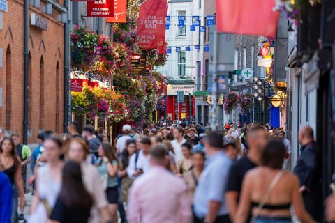 A dense crowd on a busy street with hanging baskets and flags, Dublin, Ireland