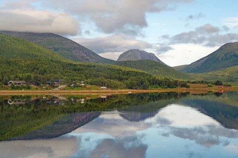 Landscape with mountains and a lake with calm reflection, surrounded by forest and small huts under