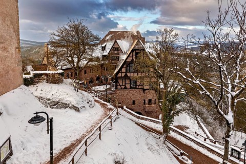 Half-timbered house in a winter landscape, surrounded by snow and trees under a cloudy sky, The