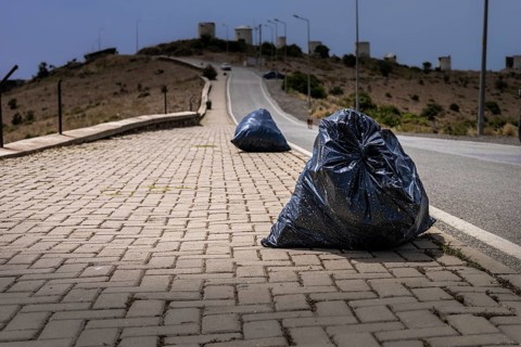 Two black garbage bags on a paved road in a barren landscape. The scene highlights environmental