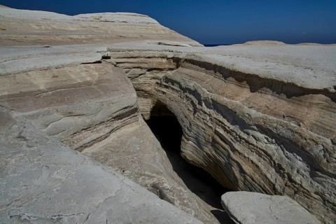 Rocky crevice and cave in dry rocky environment under clear sky, white volcanic rock, bizarre white