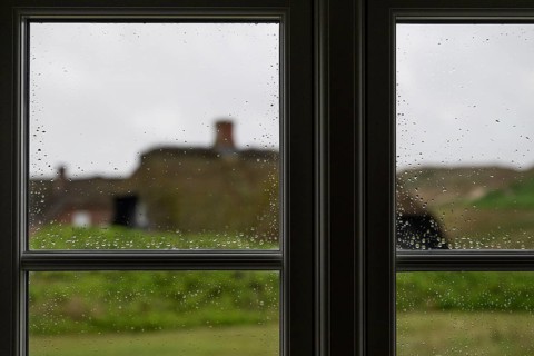 View through window panes with raindrops beading, blurred traditional thatched Danish houses in the