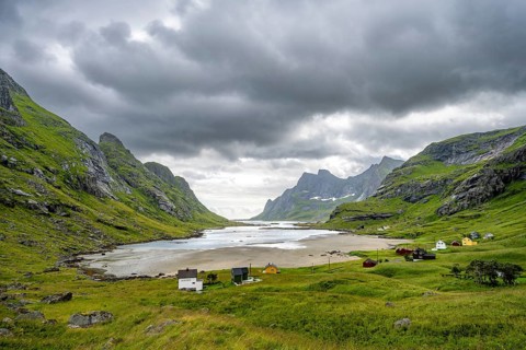 Houses on Bunesfjorden fjord, green mountain landscape and dark clouds, Lofoten, Norway