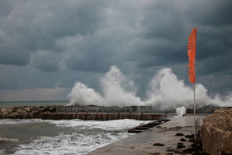 Stormy sea with high waves, grey sky and an orange flag in the foreground, Cyprus