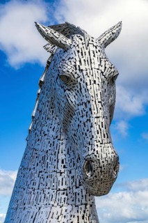 A close-up view of a Kelpie horse-head sculpture against clouds, designed by Andy Scott, one of a