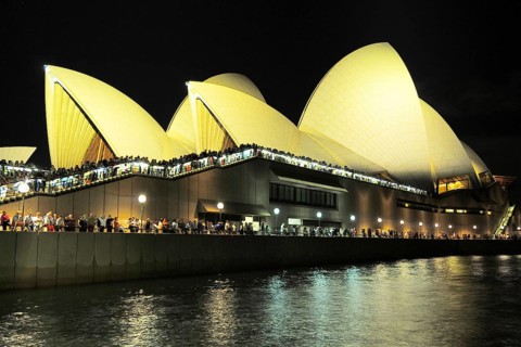 Sydney Opera at night, spectators at the railing watch the world's largest luxury liner Queen Mary