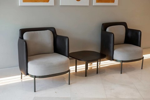 Two modern armchairs with a small table in between, set against a neutral wall. The chairs have a