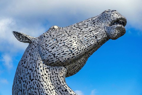 A close-up view of a Kelpie horse-head sculpture against clouds, designed by Andy Scott, one of a
