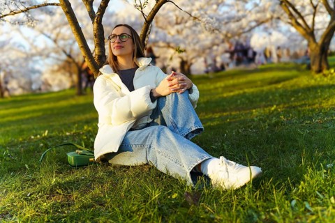 Young woman sitting on grass in blooming cherry garden and looking at sakura trees, Woman sitting