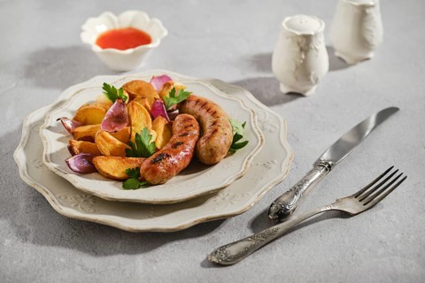 Grilled banger sausages with roasted potatoes, red onion and herbs. Small bowl with sauce sits