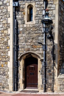 A small arched wooden doorway sits beside a mullioned window on a rubble stone wall at Windsor