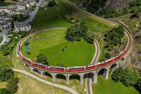 Red train of the Rhaetian railroad line, Bernina Express, passing the circular Brusio viaduct,