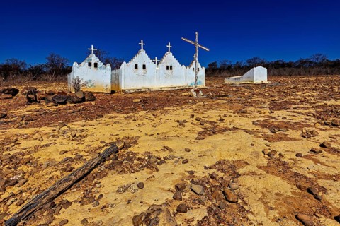 White chapel with crosses stands in a dry, rocky desert with a cloudless sky, cemetery in the