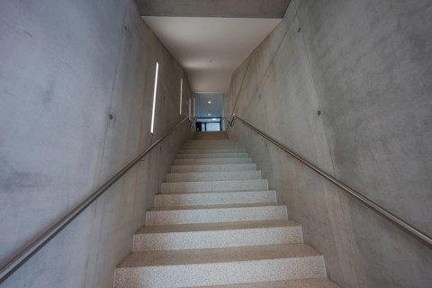 Minimalist concrete staircase flanked by geometric concrete walls, Boarding House des Klinikverbund