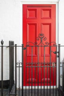 Red door behind stylized black painted metal fence in classic design, Chelsea, London, Great