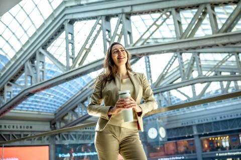 Woman in a professional suit holding a reusable coffee cup, standing confidently in a bright,