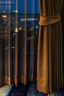 Hotel room view through curtain illuminated city scenery, Pattaya, Thailand
