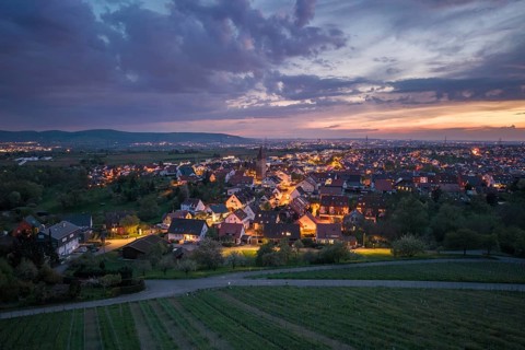 City skyline at night illuminated under a dramatic sky with a view of surrounding vineyards, Korb