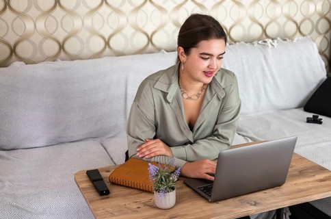 Young Caucasian woman with brown hair working on a laptop at home. She is smiling and sitting at a