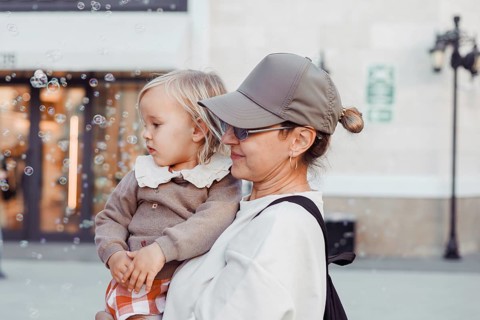 A little girl playfully points towards bubbles while being held by her smiling grandmother. They