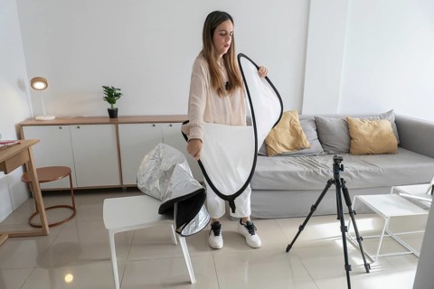 Woman standing and folding white photography diffuser reflector into black zippered carrying case,