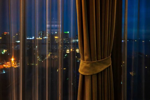 Hotel room view through curtain illuminated city scenery, Pattaya, Thailand