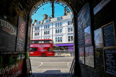 View through the archway of a historic pub onto a passing red double-decker bus, near London Bridge