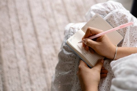 A person writes in a notebook while sitting on a carpet, conveying a relaxed atmosphere