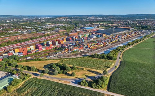 Aerial view of a large container terminal with freight trains, shipping containers, cranes, and