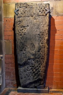 Weathered recumbent grave slab bordered with interlace carving and a later 1723 inscription, part