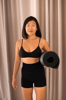 Woman standing with a yoga mat in fitness wear, exuding confidence indoors