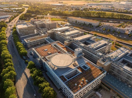 Complex of buildings in an industrial area, surrounded by trees and roads, construction site of the