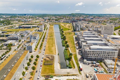 Modern urban landscape with a narrow canal and surrounding green spaces under blue skies, new