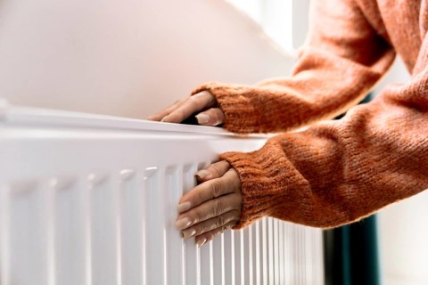 Close-up of a hand adjusting the temperature on a radiator thermostat, regulating home heating for