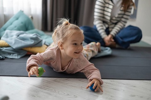 A young Caucasian girl with blonde hair plays on the floor with colorful balls. A woman in a