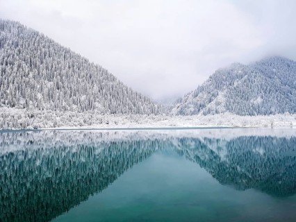 Mountains covered with trees and snow are symmetrically reflected in the turquoise water of the